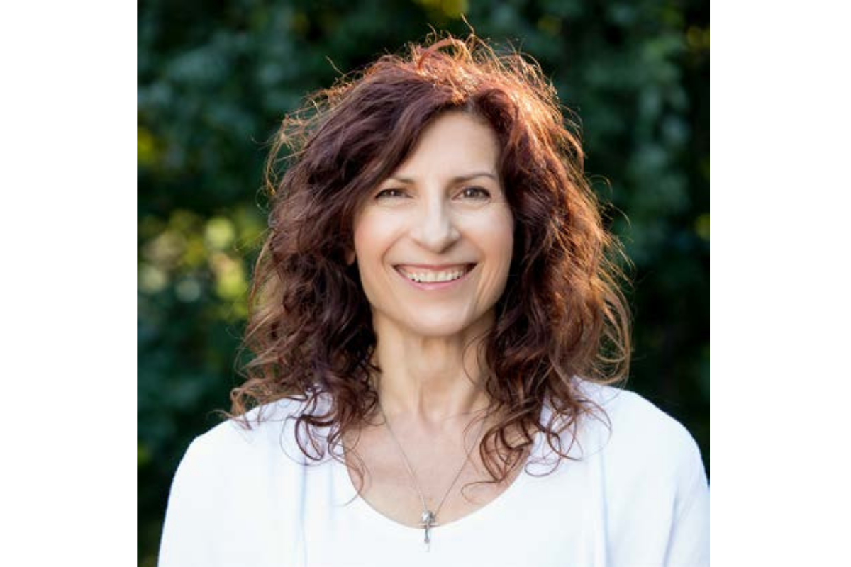 Woman with brown hair and white blouse smiles looking directly into the camera.