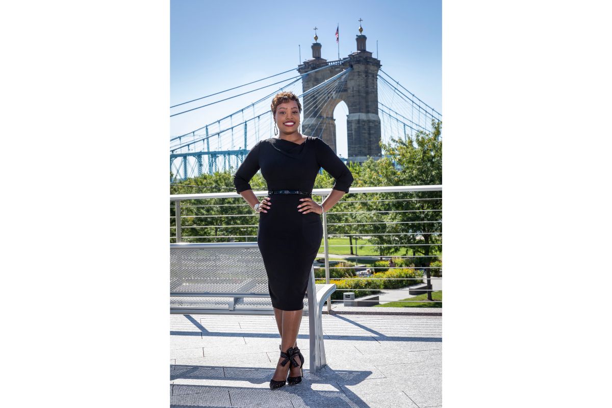 Black woman in black dress standing with hands on her hips with bridge in background