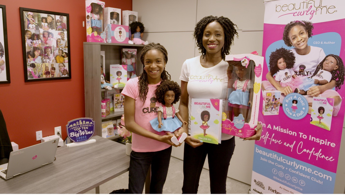 Black woman and young girl smiling and holding Black dolls.