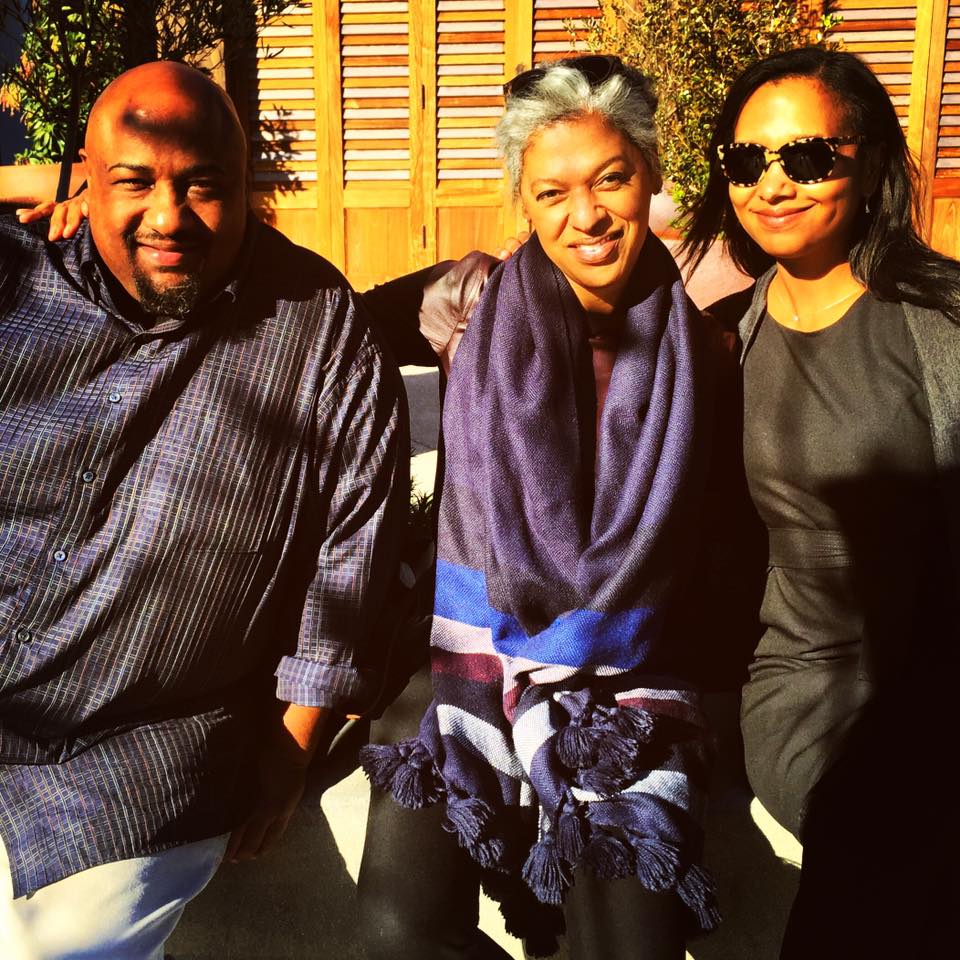A Black man and two Black women sitting together in front of a wine vineyard.