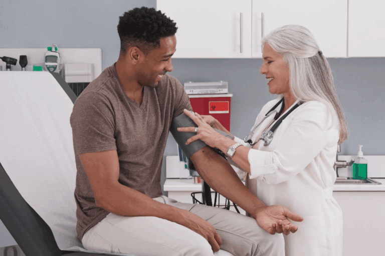 Young Black man getting his blood pressure checked by older nurse.