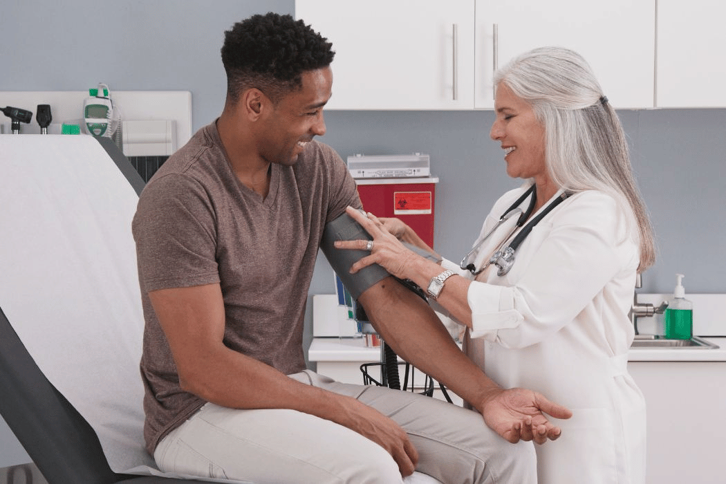 Young Black man getting his blood pressure checked by older nurse.