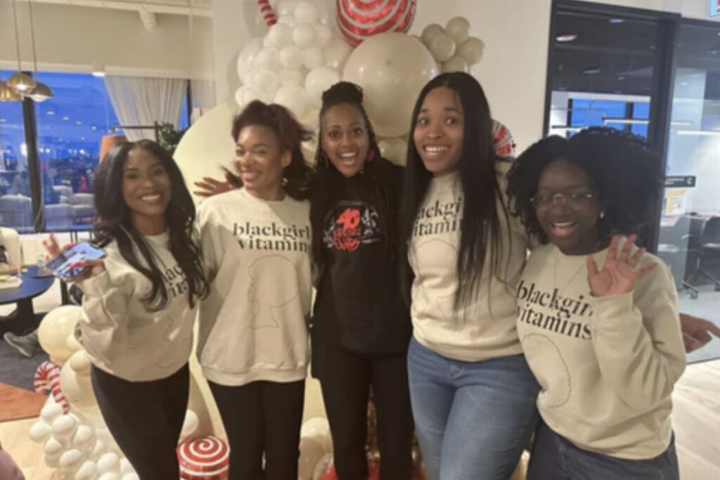 Five young Black women standing with their arms around each other smiling for the camera