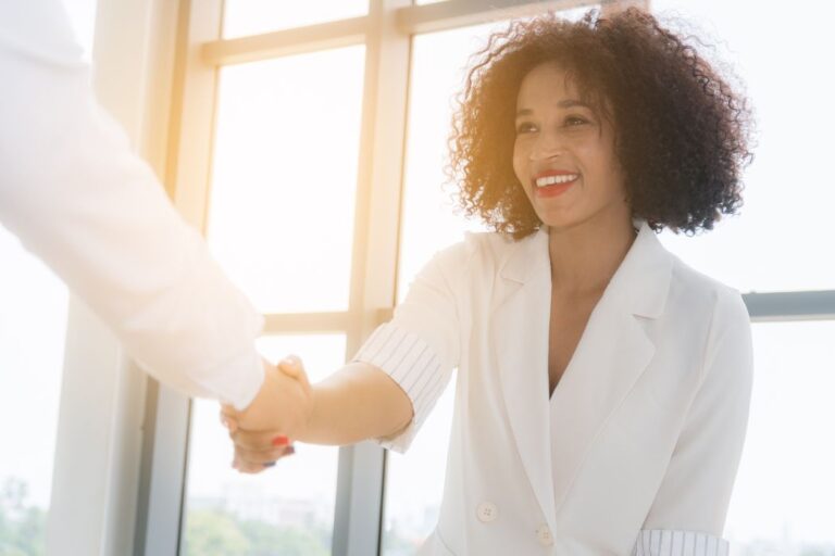 Young Black woman in white blouse shaking hands.