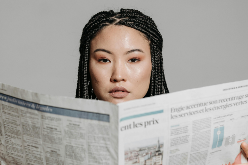 Asian woman holding an open newspaper in front of her face.
