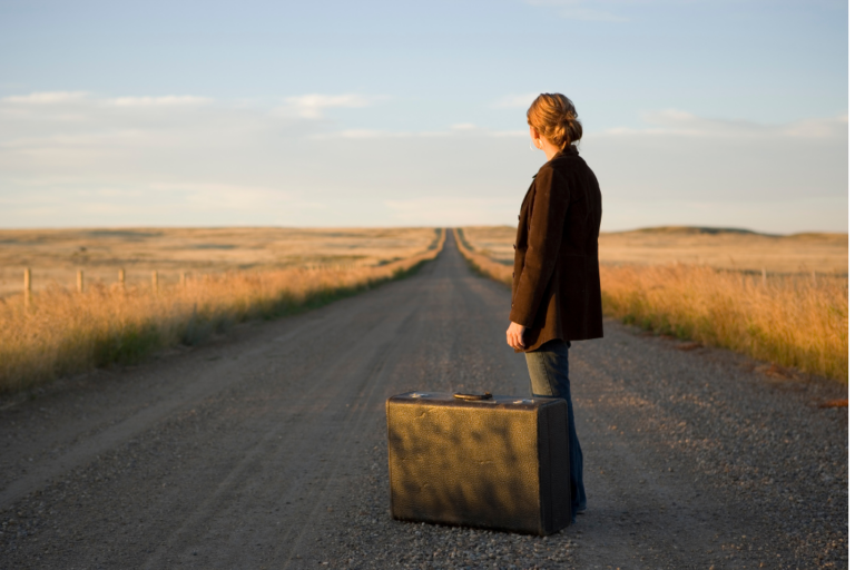 Young woman stands on an deserted road with a briefcase looking at the journey ahead of her