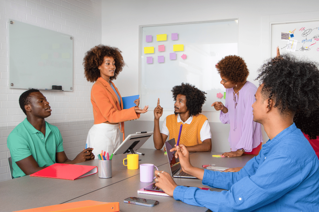 Black woman with an afro standing at whiteboard teaching colleagues
