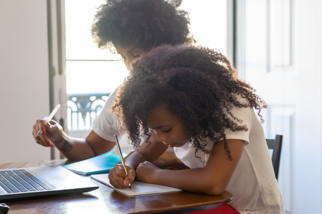 Two Black students sitting at a desk together with their heads down studying