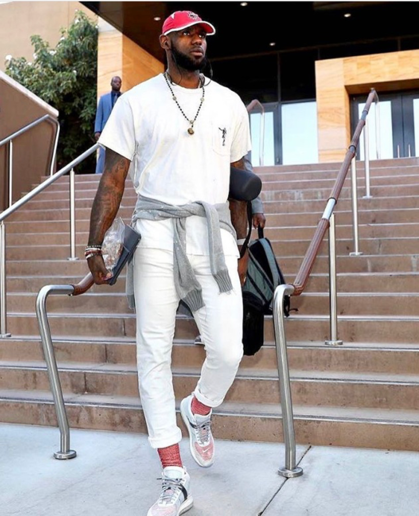 NBA player Lebron James dressed in white pants and a white t-shirt walking down steps.