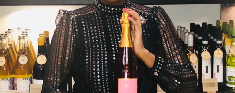 Marvina Robinson holding a bottle of champagne in front of racks of champagne bottles.