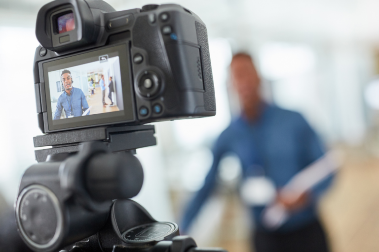 Video camera in foreground showing image of Black man being filmed.