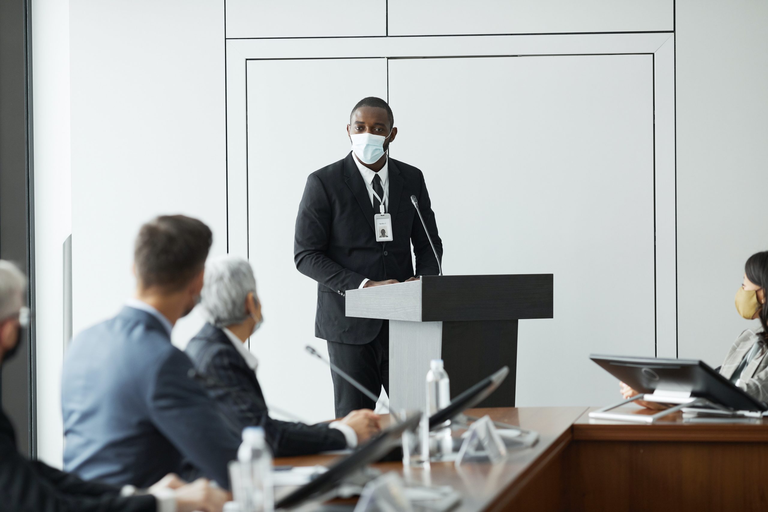 A man in a mask speaking at a meeting - Brand Safety Week Announces Inaugural DE&I Summit